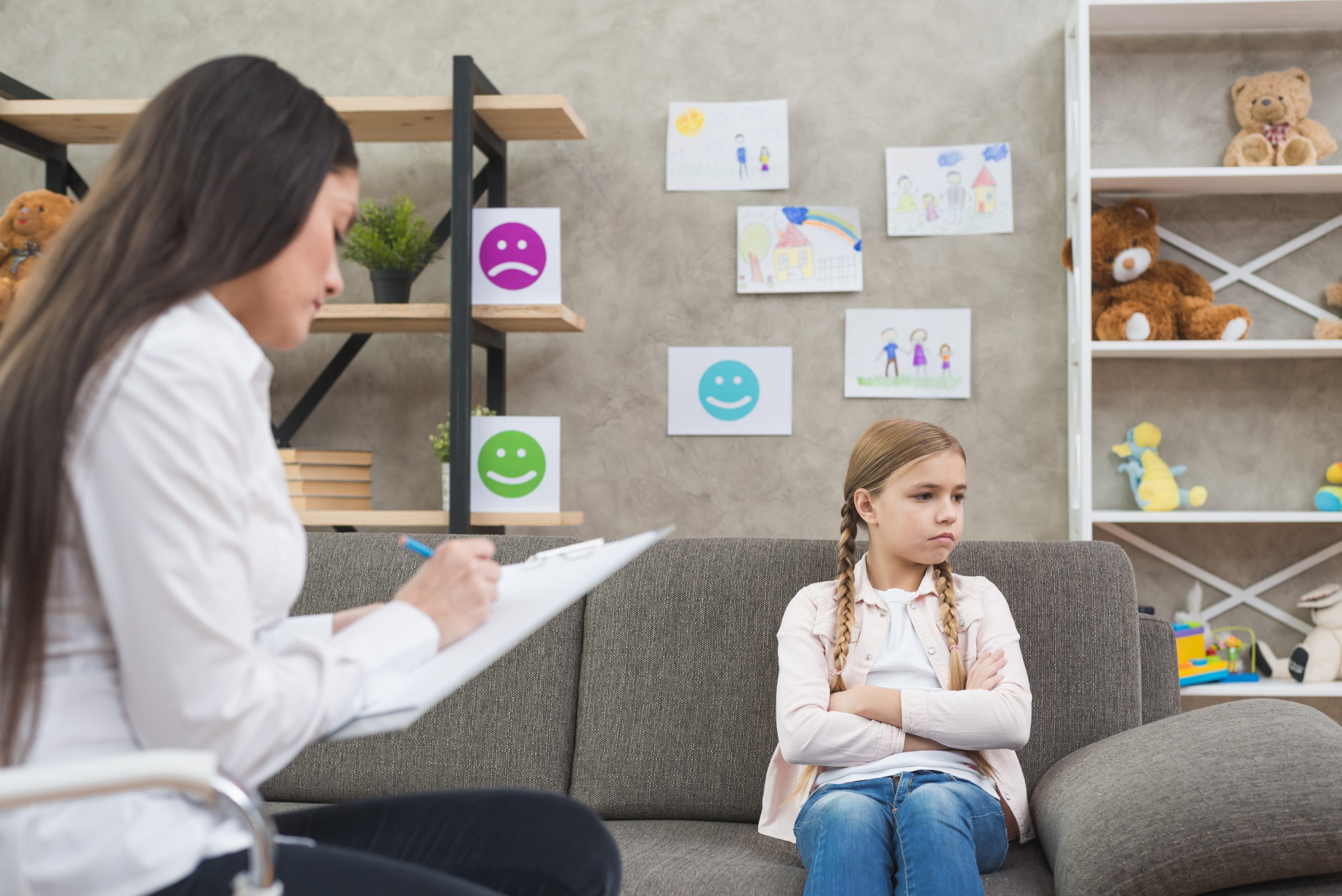 muchacha deprimida que se sienta en el sofa con la nota femenina de la escritura del psicologo en el tablero scaled